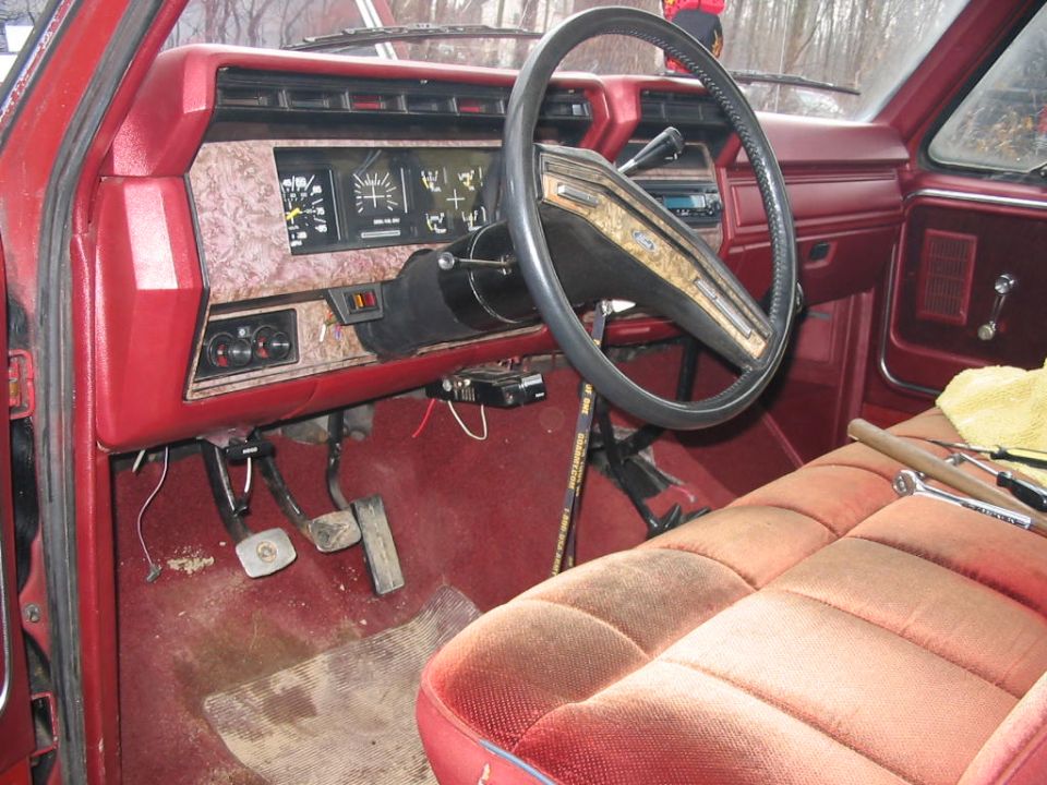 Interior of a red truck, showing the dashboard, steering wheel, pedals, and passenger seat