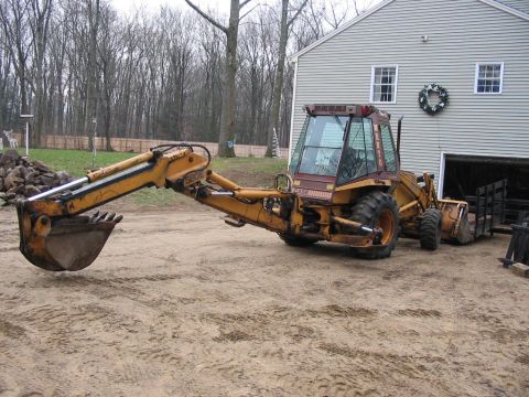 1985 Ford F-350 - A yellow backhoe loader is parked in front of a house with its boom extended, ready for work.