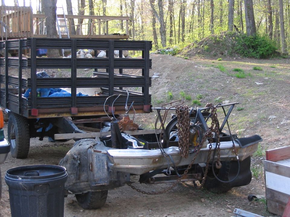 Trailer loaded with a disassembled truck frame, chains, and other parts. A black trash can is in the foreground