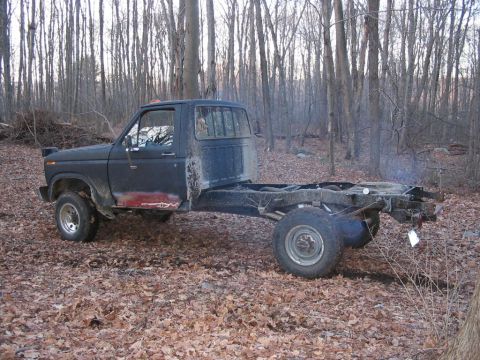 1985 Ford F-350 - This Ford pickup truck is missing its bed and appears to be in a wooded area.