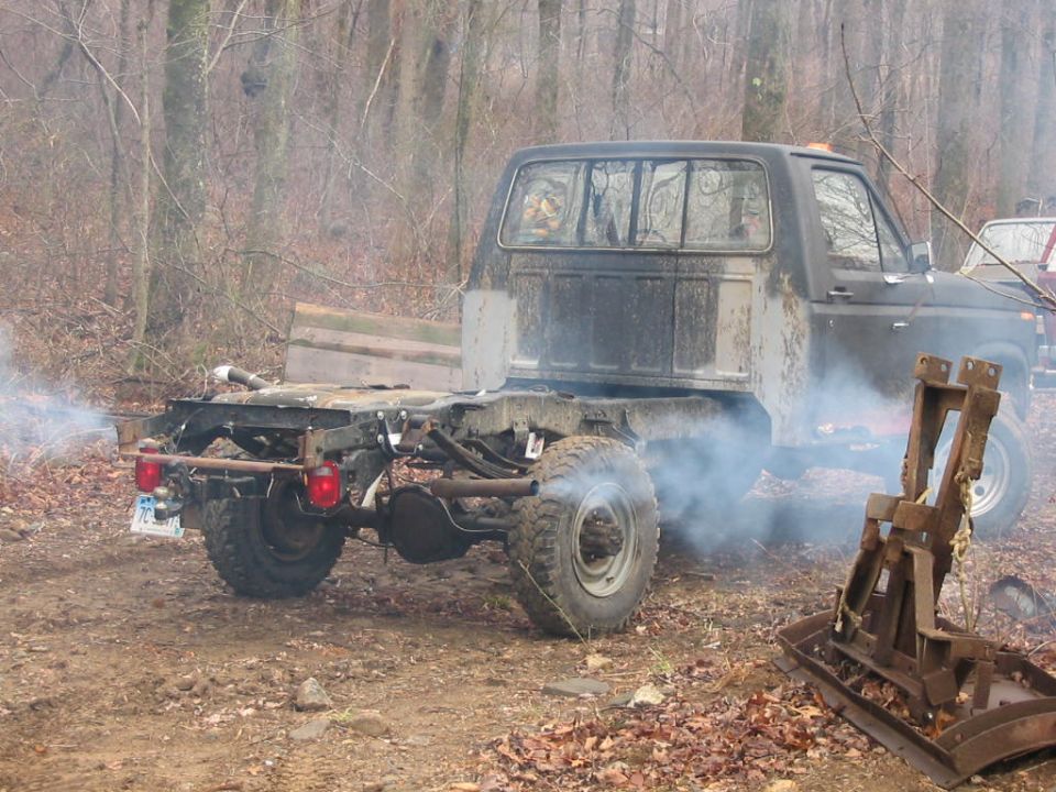 Rear view of a 1985 Ford F-350 pickup truck with exposed frame and exhaust emitting smoke