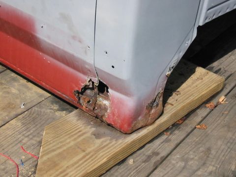 1985 Ford F-350 - The lower body panel of a truck shows extensive rust and damage, with red primer visible.