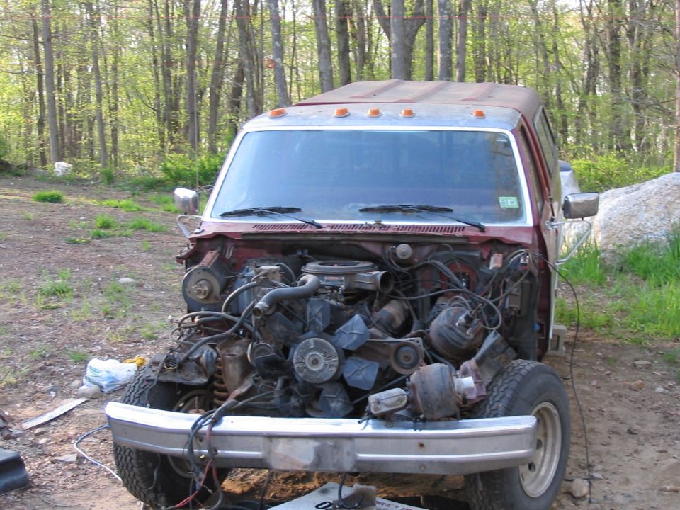 Ford truck missing its engine, parked outside with trees in the background