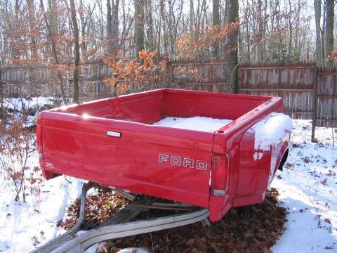 1985 Ford F-350 - This red Ford pickup truck bed with dual rear wheels is mounted on a trailer in a snowy outdoor setting.