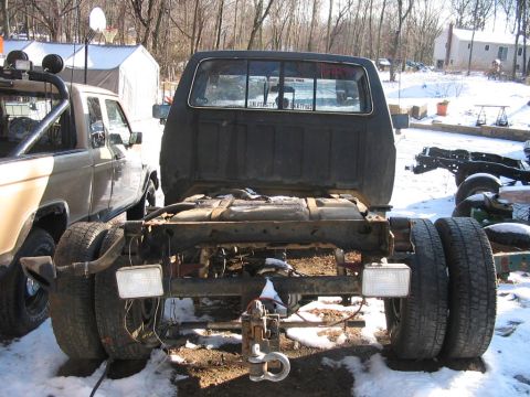 1985 Ford F-350 - The rear of a truck chassis is shown with dual wheels and a large fuel tank. Another truck is visible to the left.