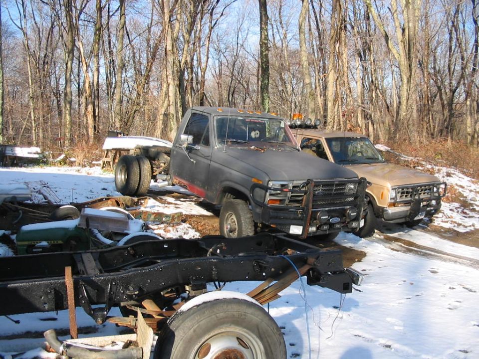 Tan Ford Ranger with a dark gray truck in front, parked in a snowy wooded area