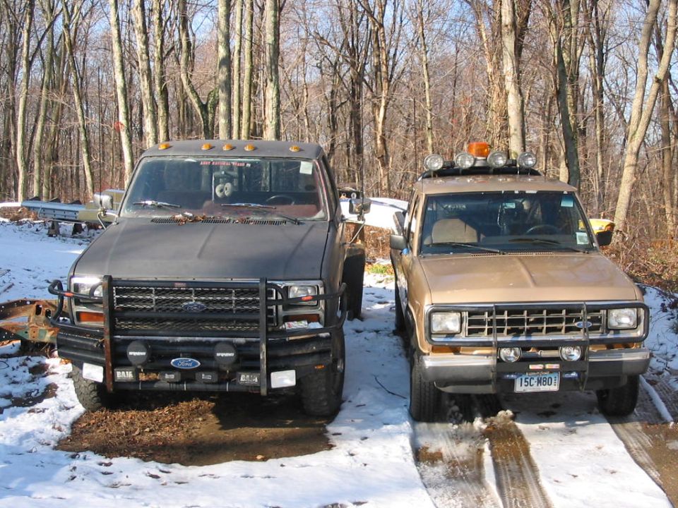 Two Ford trucks, a tan Ranger and a dark gray larger truck, parked in a snowy wooded area