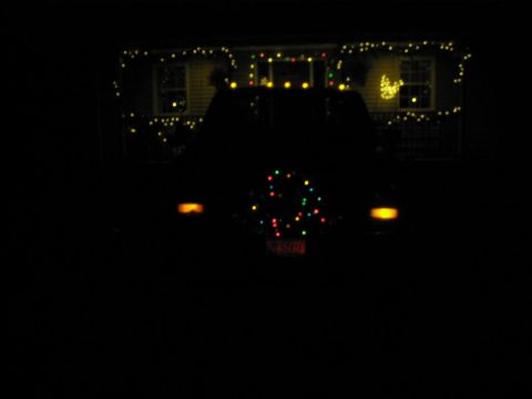 1985 Ford F-350 - SUV's rear is decorated with Christmas lights, including on the spare tire cover. The house in the background is also lit up.