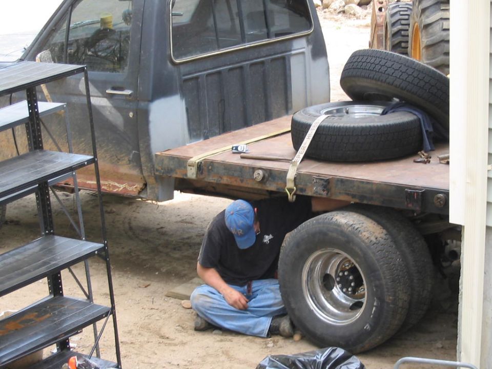 Man working beside dual rear wheels of dark blue Ford flatbed pickup