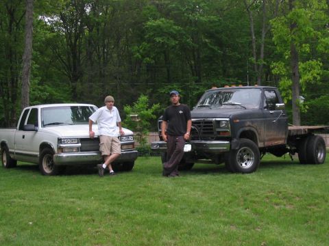 1985 Ford F-350 - A black flatbed truck with dual rear wheels is parked on a grassy lawn next to a white pickup truck.