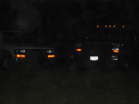 1985 Ford F-350 - Two trucks are visible at night, with their headlights illuminated.