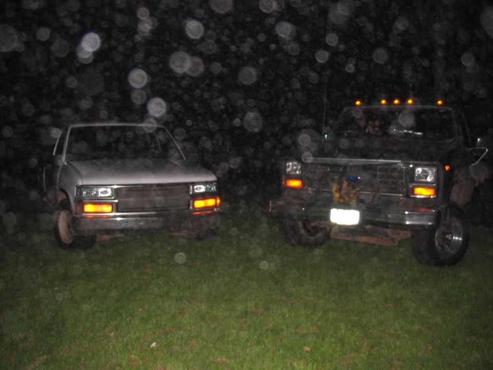 Two pickup trucks parked on grass at night with headlights on