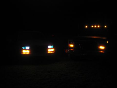1985 Ford F-350 - Two trucks are parked at night, their headlights illuminating the darkness.