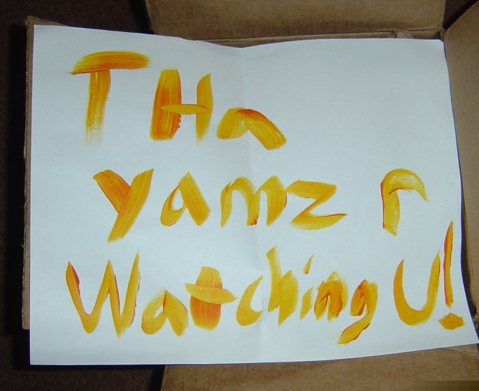 Handwritten note with orange paint saying 'Tha Yamz r Watching U!'