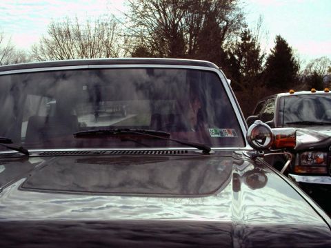 1984 Ford Bronco - A dark gray Ford Bronco is seen from the front, with another vehicle partially visible behind it.
