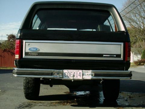 1984 Ford Bronco - The rear of a black Ford Bronco is shown, a chrome bumper and a silver accent panel on the tailgate.