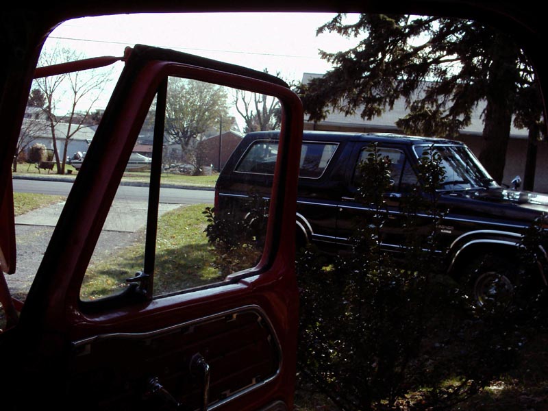 Dark blue SUV with chrome trim parked on a grassy lawn, viewed from inside a red vehicle