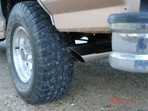 1995 Ford Bronco - Close-up view of the rear wheel, exhaust, and bumper of a tan SUV, showing off its off-road tire.