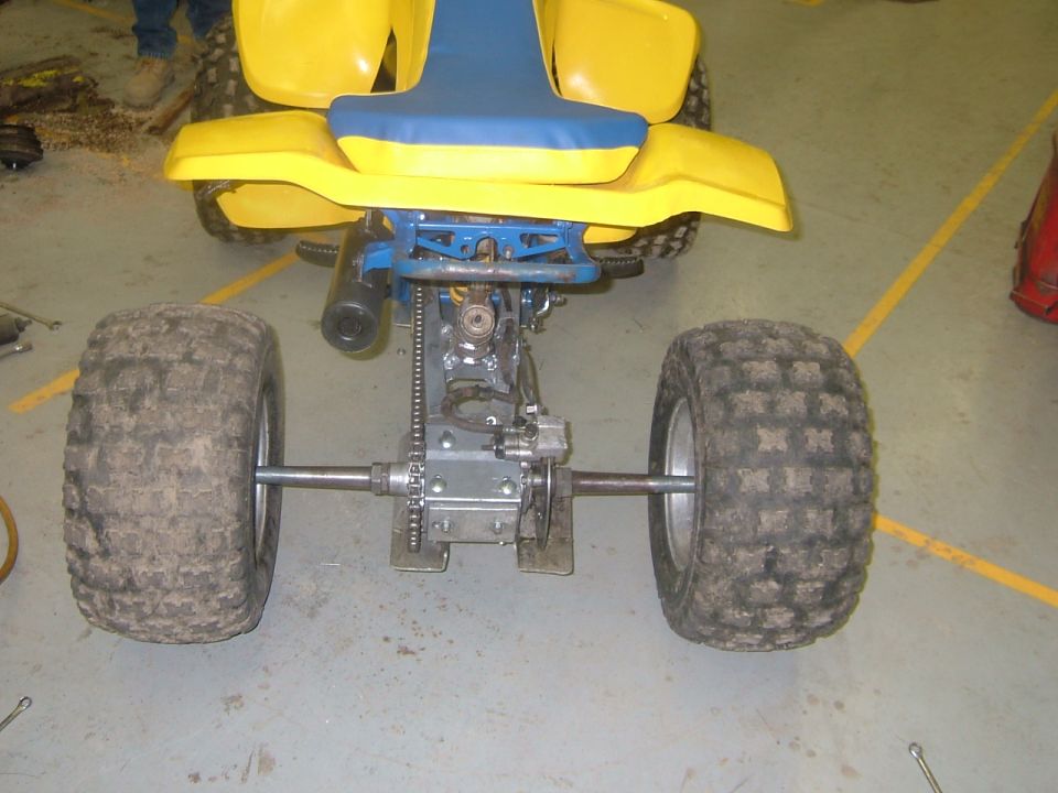 Rear view of a yellow and blue ATV showing its axle, chain drive, and knobby tires