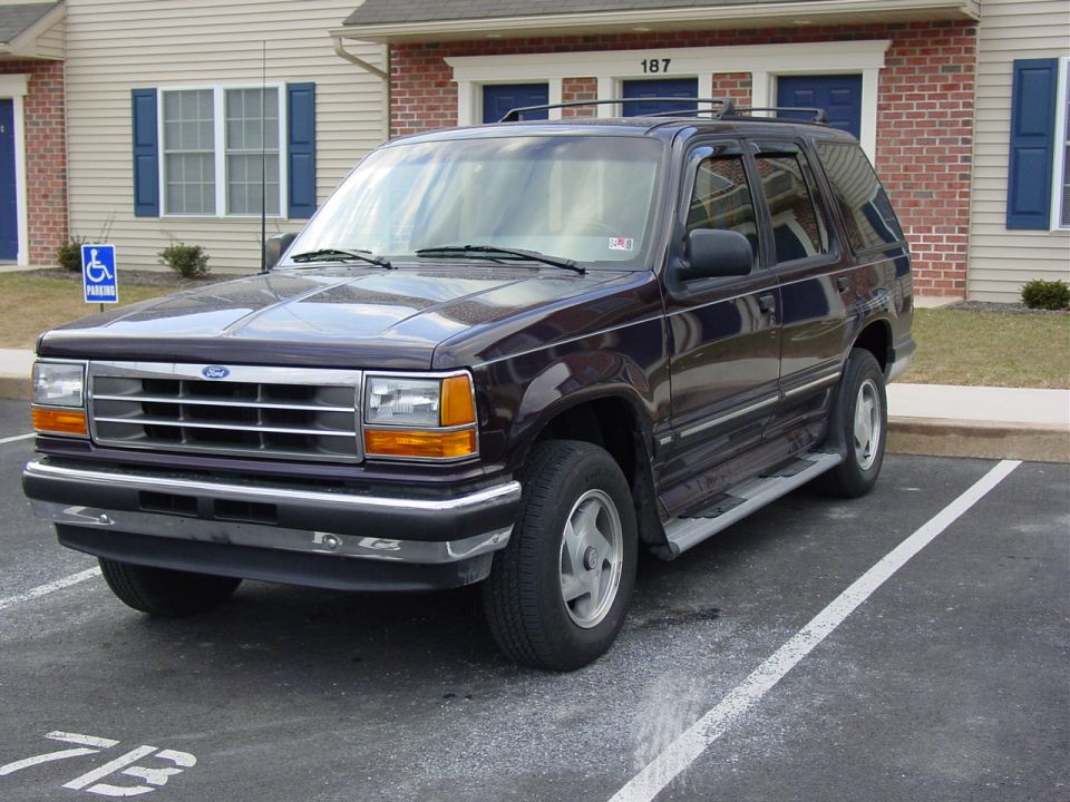 Dark purple first-gen Ford Explorer parked in front of a brick building