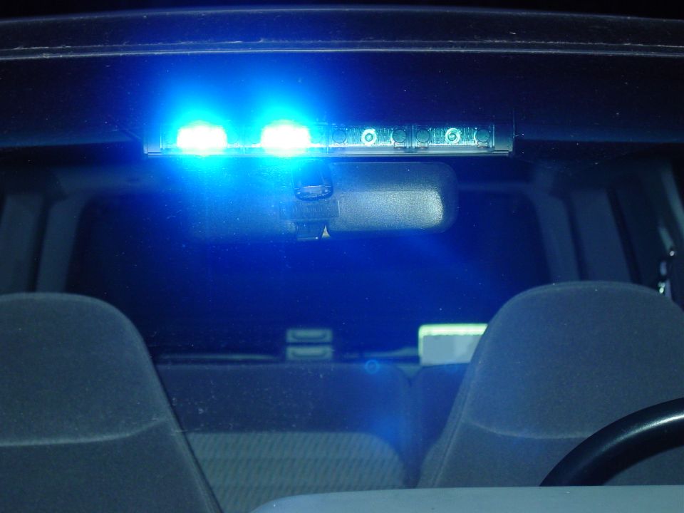 Interior LED visor light bar flashing blue above rear-view mirror at night, gray seats below