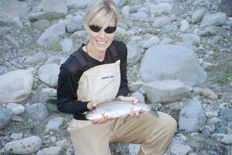 1994 Ford Bronco - A smiling woman proudly displays a freshly caught fish while kneeling on a rocky riverbank.
