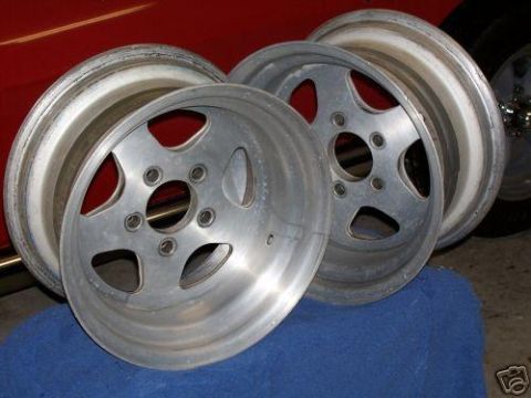 2005 Ford Mustang - A set of three aluminum wheels are shown, with a red car body visible in the background.