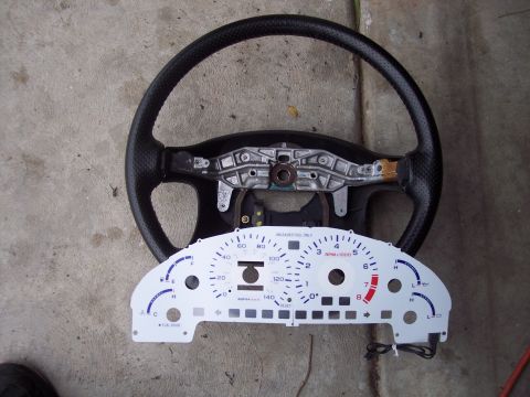 1995 Ford Probe - Vehicle steering wheel and instrument cluster laid out on a concrete surface.
