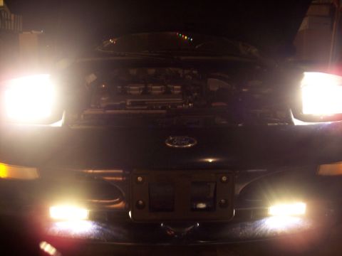 1995 Ford Probe - The front of a Ford vehicle is illuminated by its headlights, with the hood raised to reveal the engine.