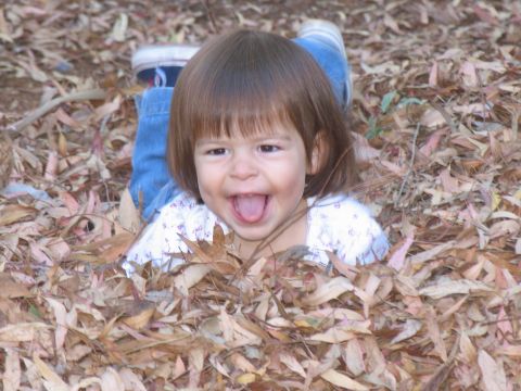 1984 Ford Bronco - A happy child is buried in a pile of fallen leaves, with only their head and shoulders visible.