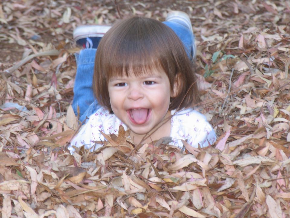 Child lying in autumn leaves, sticking tongue out