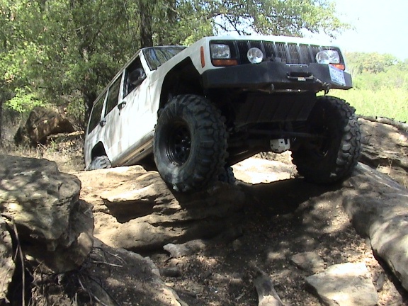 White Jeep Cherokee climbing over rocks on a trail