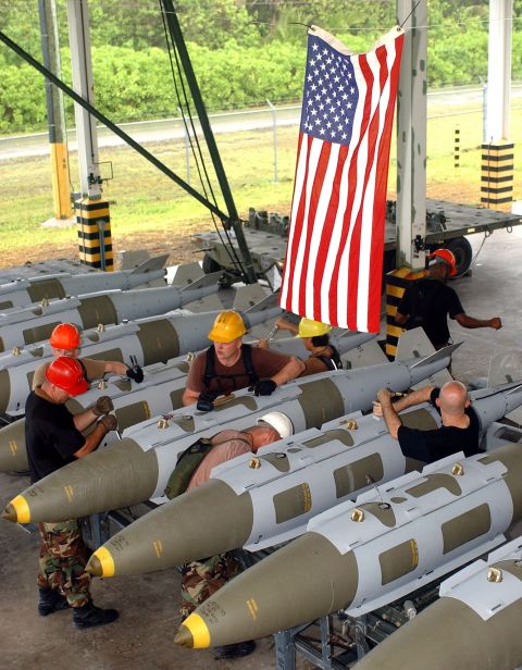 1981 Ford Bronco - Workers prepare ordnance under a large American flag, suggesting a military or training exercise.