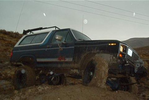 1986 Ford Bronco - This lifted Ford Bronco is deeply embedded in mud, with its front tires struggling for traction.