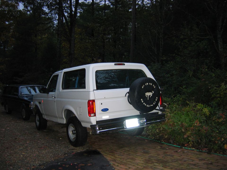 1995 Ford Bronco XL parked next to a dark SUV, spare tire mounted on rear door