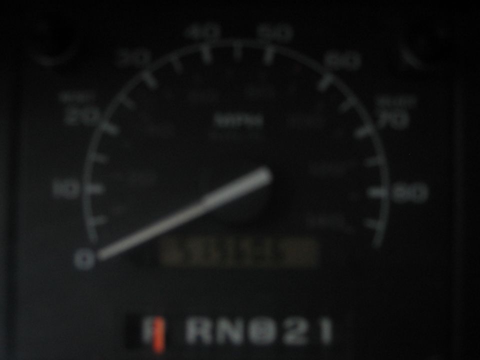 Blurry speedometer at 0 MPH with odometer and PRND21 gear indicator in a dark dash cluster