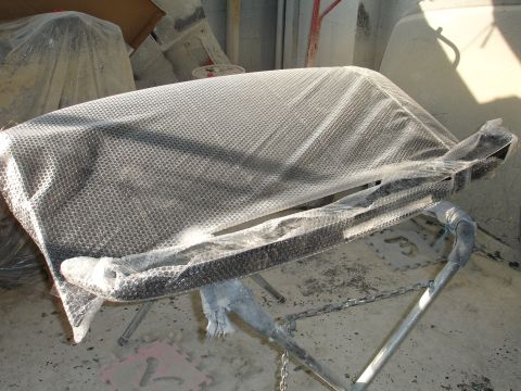 1993 Ford Taurus - A car bumper is covered in protective wrapping and placed on a stand in a dusty workshop environment.