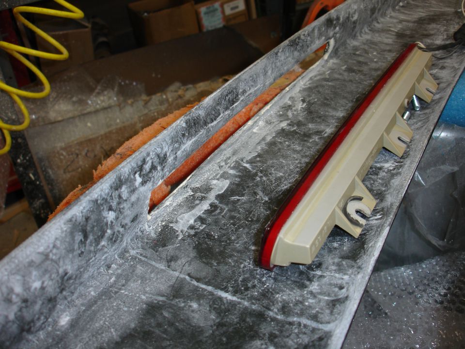Car part with red light strip and mounting brackets, in a workshop setting