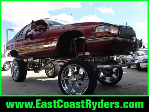1994 Ford Bronco - Maroon full-size Buick sedan lifted extremely high on an exposed tube-link suspension over huge chrome multi-spoke wheels, with a person le…