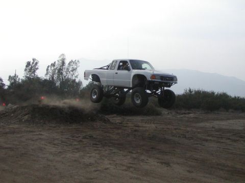 1984 Ford Bronco - Pickup truck airborne during an off-road event, kicking up dust.