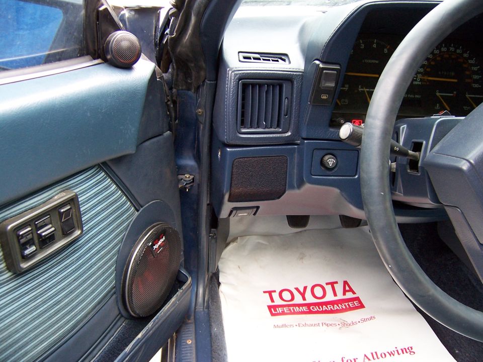 Blue interior of a Toyota with aftermarket door speaker and Toyota Lifetime Guarantee paper floor mat