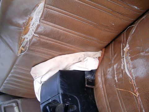 1986 Ford F-250 - The interior of a vehicle shows worn brown vinyl seats and a black center console with a white cloth covering part of it.