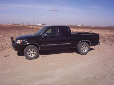 2003 Toyota Tundra - A black 2003 Toyota Tundra pickup truck is parked on a dirt road with a dry field in the background.