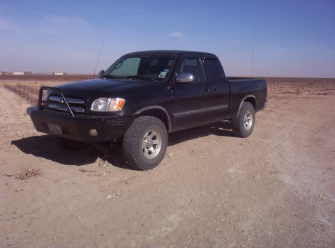 2003 Toyota Tundra - This black 2003 Toyota Tundra pickup truck is equipped with an aftermarket bumper and bull bar, seen parked on a dirt road under a clear bl…
