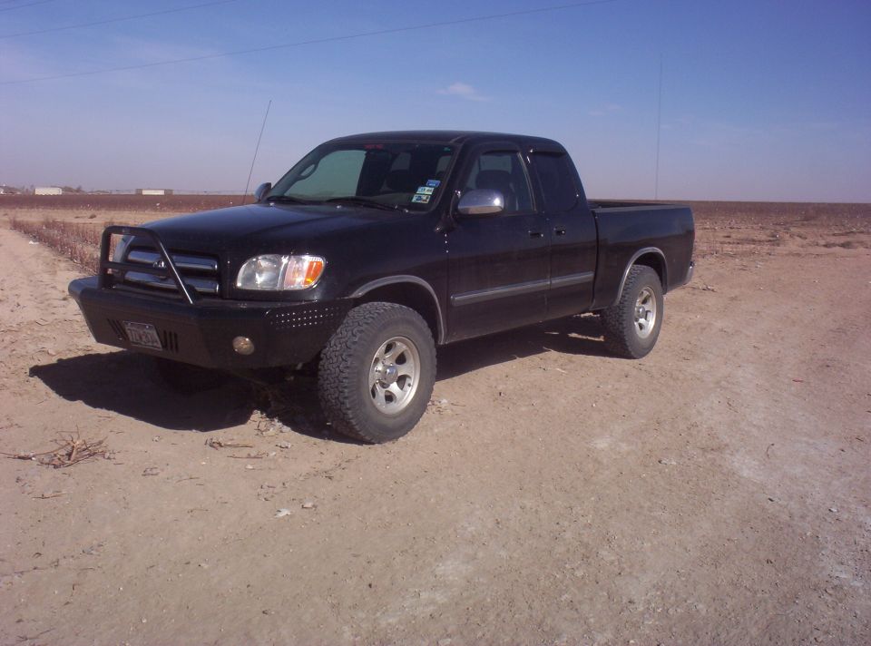 Black Toyota Tundra extended cab pickup with brush guard parked on dirt beside a field