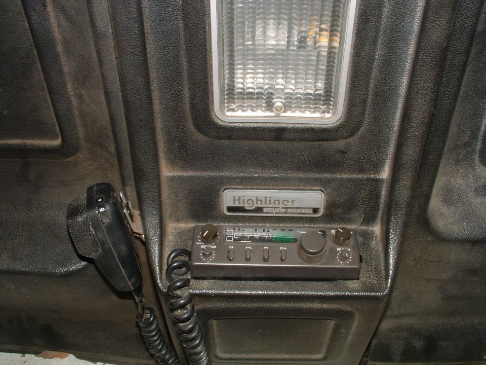 Overhead CB radio and mic below a dome light on a textured cab panel