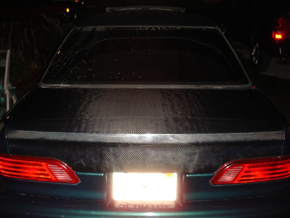 Dark green car's rear with carbon fiber trunk lid and horizontal taillights