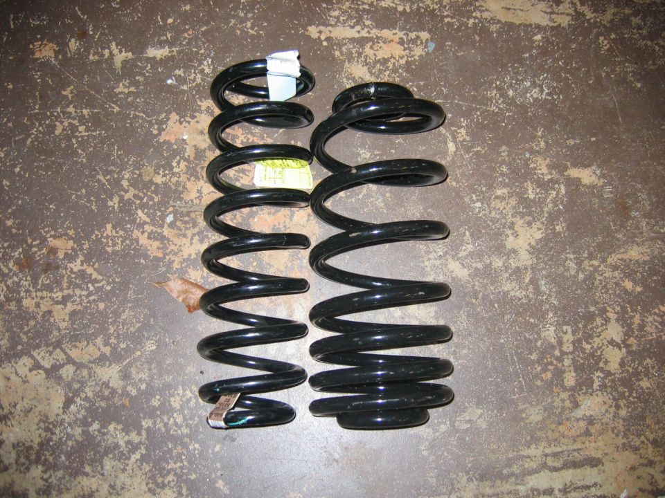 Two black coil springs on a concrete floor. One spring is taller than the other