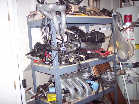 1995 Ford Probe - Various engine components are organized on shelving units in a garage.