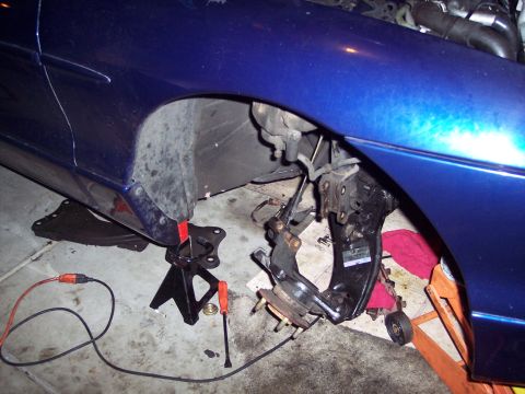 1995 Ford Probe - Front suspension components are removed from a blue car, supported by jack stands, with a website URL visible in the lower right corner.